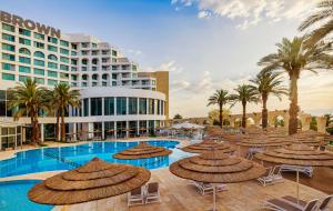 a hotel with straw umbrellas and a swimming pool at Brown Dead Sea By Brown Hotels in Ein Bokek