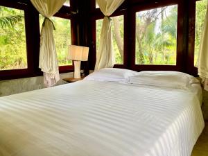 a bedroom with a large white bed with windows at Latehouse bar Amphawa in Amphawa