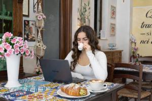 a woman sitting at a table with a laptop and a cup of coffee at B&B Gi-Rosa Caltagirone in Caltagirone