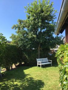 a white bench sitting in the grass under a tree at Ferienhaus Familie Lehmann in Borkum