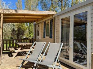 two white folding chairs on a deck next to a cabin at Camping Le Neptune in Lanloup