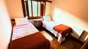 two beds in a room with a window at Espaçoso Apto triplo a 300 mts do Centrinho Capivari in Campos do Jordão