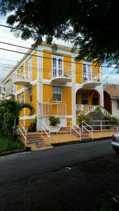 a large yellow building with white railings on a street at St. James Guesthouse in Roseau