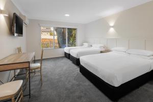 a hotel room with two beds and a desk and a television at Elizabethan Lodge in Melbourne
