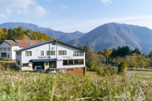 a large white house with mountains in the background at 北国ロッヂ in Otari