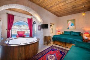 a bedroom with a tub and a bed and a bed and a tv at Megaron Cave Hotel Cappadocia in Ortahisar