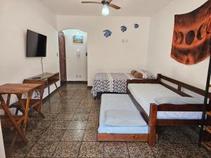 a room with two beds and a table and a television at Suíte Rodoviária no centro de Arraial in Arraial do Cabo