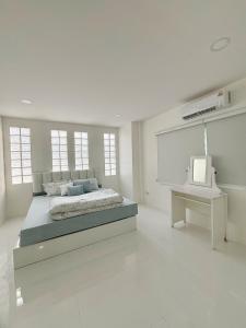 a white bedroom with a bed and a tv at Whitebeach Cottage in Chon Buri