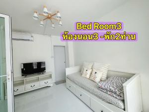 a white bedroom with a bed and a television at Whitebeach Cottage in Chon Buri
