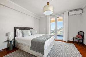 a white bedroom with a bed and a large window at Villa Vineyard by Homie in Câmara de Lobos