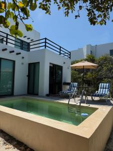 a pool with two chairs and an umbrella next to a house at Casa Nora in Sisal