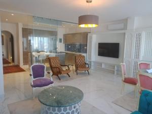 a living room with chairs and a table and a tv at L'appartement en face de la baie in Sidi MʼHamed