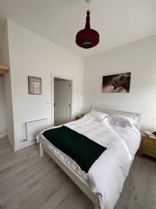 a white bedroom with a large bed with a green blanket at Carpenters Cottage in Rathvilly