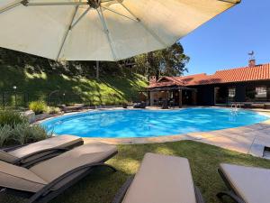 a swimming pool with chairs and an umbrella at Casa 05 Vale Boa Vista - Refúgio Moderno em Condomínio Exclusivo in Teresópolis