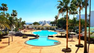a large swimming pool with palm trees in a resort at Bungalow Alma Playa Roca in Costa Teguise