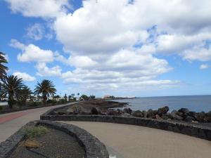 a walkway next to the ocean with trees and rocks at Bungalow Alma Playa Roca in Costa Teguise