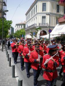 a group of musicians in red uniforms walking down a street at Metropolis Hotel in Athens