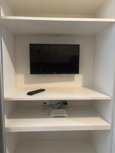 a tv on a white shelf with a remote control at Estúdio Fit Caiobá - Matinhos in Matinhos