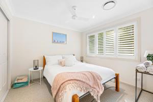 a white bedroom with a bed and a window at Bec's Beach House Getaway in Batemans Bay