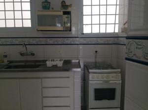 a white kitchen with a sink and a stove at Pitangueiras Frente Total Mar pé na areia in Guarujá +16 photos