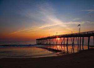 a pier on the beach with the sun setting at __Kristian’s Palace Your Beach Getaway in Kill Devil Hills