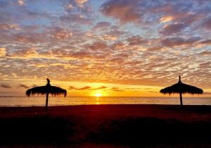 two straw umbrellas on the beach at sunset at Cabaña Rústica en Papudo in Papudo