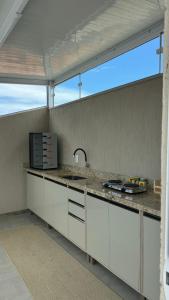 a kitchen with white cabinets and a large window at Apartamento de 2 quartos no centro de Garopaba in Garopaba