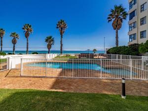 a fence around a pool with palm trees and a building at 75 Cap D'Azur in Strand