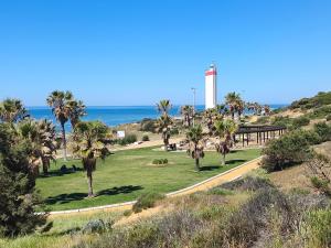 a park with palm trees and a lighthouse on the beach at Vistaluz playa in Matalascañas