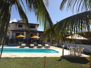 una piscina con sillas y sombrillas frente a una casa en Pousada Recanto dos Coqueiros, en Barra do Cunhau