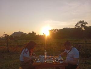 two people sitting at a picnic table with the sunset in the background at The Classic Crown Sigiriya in Sigiriya