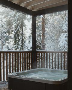 a hot tub on a deck with snow covered trees at NOA VILLAS Aurora Lapland Resort in Takala