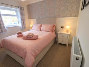 a bedroom with a bed with pink sheets and a window at Yew Tree Cottage in Wigton