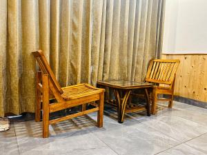 two wooden chairs and a table in front of a curtain at Tirthan Villa Homestay in Banjār