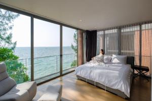 a woman sitting on a bed in a room with windows at Sandbox Beachfront Villa 6 in Ban Krathing Lai