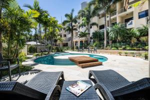 a patio with chairs and a swimming pool with palm trees at Mirra Chana Beachfront Apartments Mooloolaba in Mooloolaba