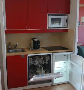 a small kitchen with red cabinets and a microwave at Maison, proche parking, piscine chauffée, en résidence, 4 ou 5 pers, RDC, lac, nature et pêche in Monflanquin