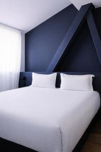 a bedroom with a large white bed with a blue wall at ClapClap Hôtel Strasbourg in Strasbourg