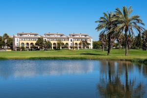 a large white building with palm trees and a pond at Barceló Costa Ballena Golf & Spa in Costa Ballena