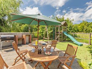 a patio with a table and an umbrella and a playground at 3 Bed in Winkleigh oc-1450b in Iddesleigh