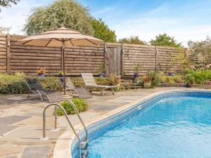 a swimming pool with an umbrella and chairs next to a fence at 3 Bed in Lifton oc-tcoah in Broadwoodwidger