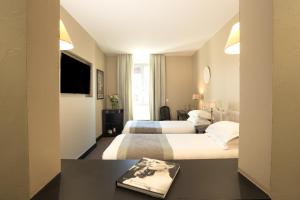 ein Hotelzimmer mit zwei Betten und einem Tisch mit einem Buch in der Unterkunft Le Cavendish in Cannes