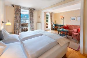 a bedroom with a large white bed and a living room at Seehotel Enzian in Weissensee