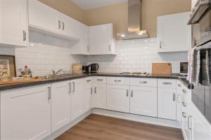 a white kitchen with white cabinets and wooden floors at Pools Cottages - Warwick Luxury Countryside Near NEC in Kenilworth