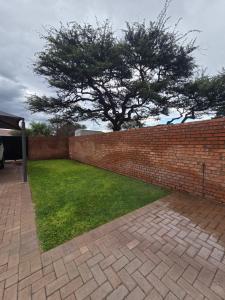 a brick wall with a yard with a tree behind it at The Oak GuestUnit in Kathu