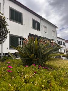 a white building with green shuttered windows and flowers at Azor International House in Ponta Delgada