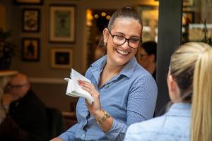 a woman is smiling while holding a book at The Chalk Hare, Royston, Hertfordshire - Acorn Pubs in Royston