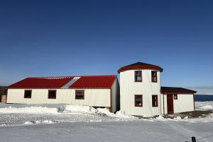 a white building with a red roof in the snow at Svalbarð guesthouse in Hvammstangi