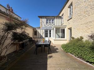 a patio with a table in front of a building at Embruns maison spacieuse rénovée 5 ch 3 sdb 2 WC belle terrasse aménagée barbecue à 250 m de la plage en plein centre d' Arromanches, tous commerces, restaurants, au coeur des plages du débarquement, proximité de Bayeux in Arromanches-les-Bains