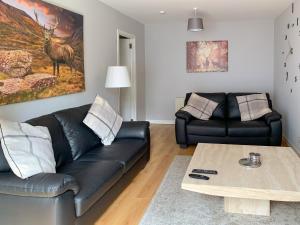a living room with a black leather couch and a coffee table at Crossburn Hideaway in Helensburgh